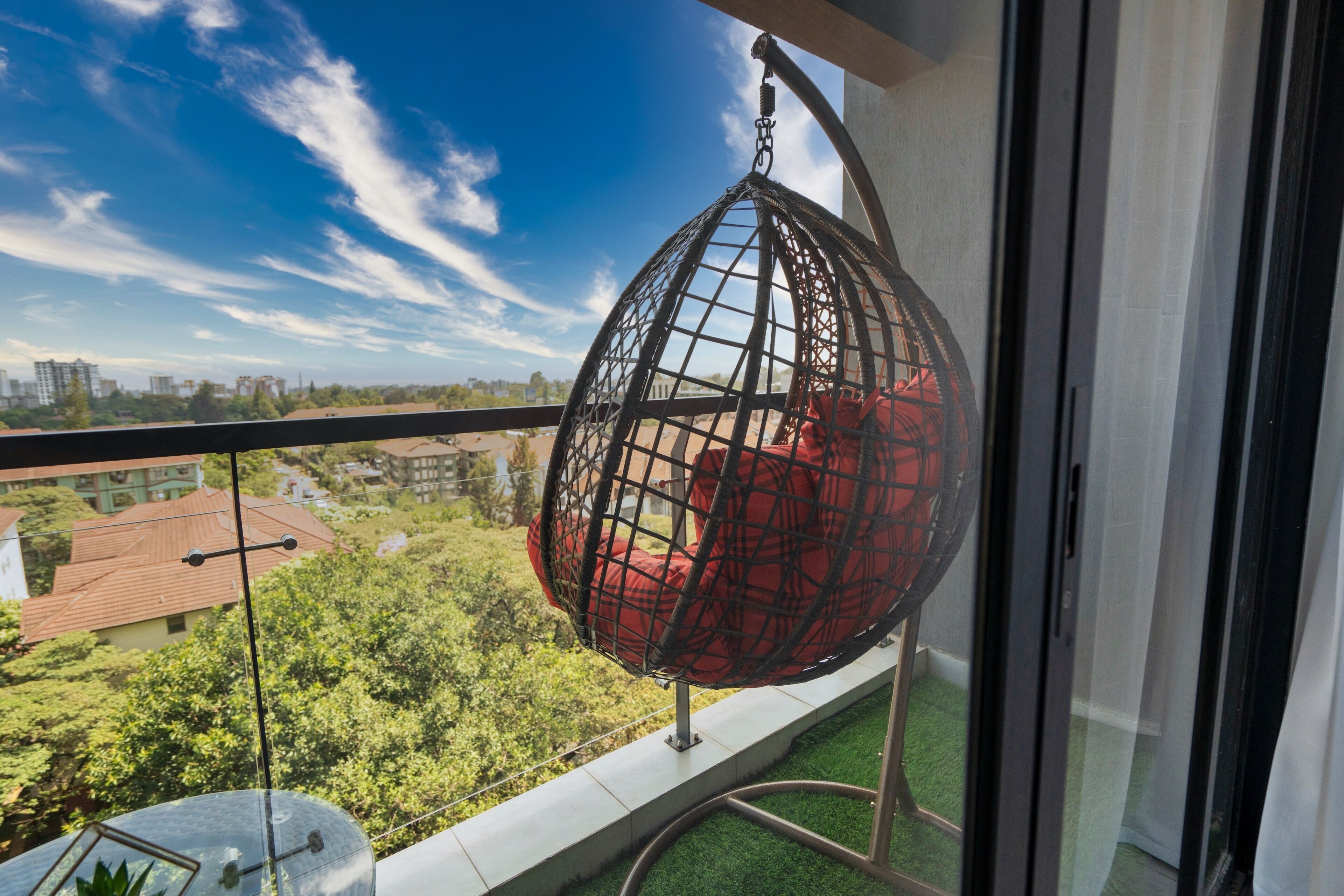 Un balcón con una hamaca colgante, un telescopio y vistas a edificios y vegetación.