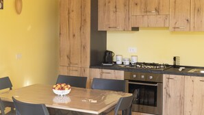 A kitchen with wooden cabinets, a dining table with chairs, and a fruit bowl. - Hillside village just minutes from the sea, ideal for escaping the daily hustle and bustle (San Floro)
