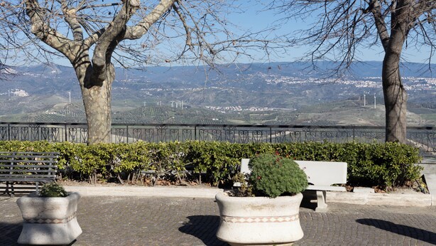 A paved walkway with benches, potted plants, and a metal fence overlooking a valley with wind turbines. - Hillside village just minutes from the sea, ideal for escaping the daily hustle and bustle (San Floro)