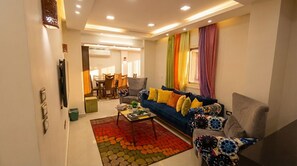 A modern living room with a sofa, armchairs, a coffee table, and a dining area in the background.