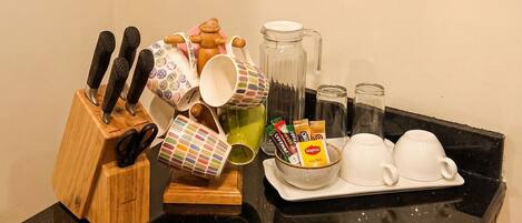 A kitchen counter with a knife block, mugs, a coffee maker, and a painting of a sunset.