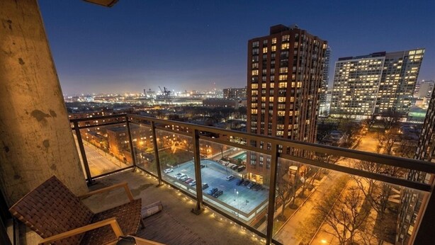A balcony with a view of a cityscape at night, including buildings and a parking lot. - Grant Park 2BR Condo with Balcony Skyline View & Gym (Chicago)