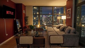 A modern living room with a large window overlooking a cityscape, a flat-screen TV, a sofa, and a dining area. - Grant Park 2BR Condo with Balcony Skyline View & Gym (Chicago)