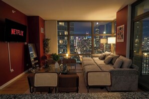 Ein modernes Wohnzimmer mit großem Fenster und Blick auf die Stadt, einem Flachbildfernseher, einer Couch und einem Essbereich.