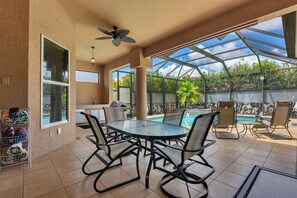 A covered patio with a glass ceiling, a round table with chairs, a ceiling fan, and a pool in the background. - Easy Living Pool House – Relax, Swim, Enjoy (Cape Coral)