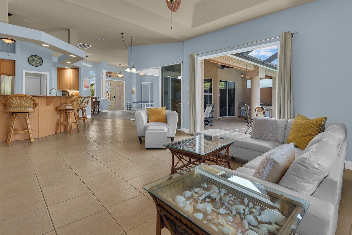 A spacious living area with a glass coffee table, white sofas, and a dining area with wicker chairs.