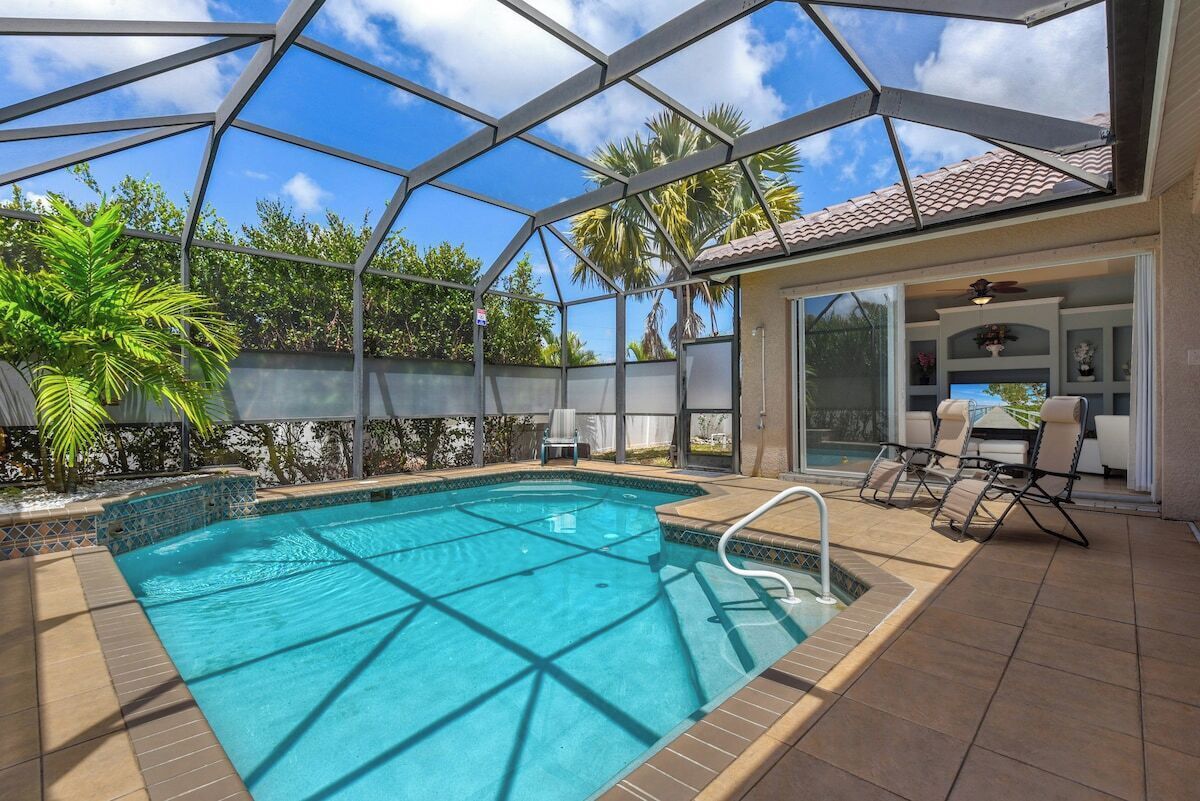 A swimming pool with a glass enclosure, surrounded by outdoor furniture and palm trees.
