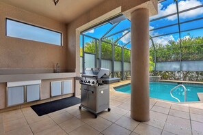 A kitchen with a built-in grill, a window, and a pool view. - Easy Living Pool House – Relax, Swim, Enjoy (Cape Coral)