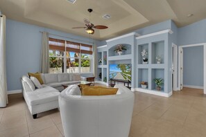 A living room with a white sofa, a ceiling fan, and a view of the outdoors. - Easy Living Pool House – Relax, Swim, Enjoy (Cape Coral)