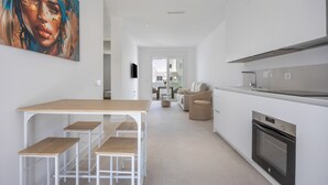 A modern kitchen with white cabinetry, a built-in oven, and a dining area with a wooden table and stools. - Apartment 'Los Drogos, Building A, First A' with Shared Pool, Garden and Wi-Fi (Chiclana de la Frontera)