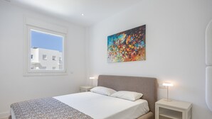 A bedroom with a bed, a window, a painting, and bedside lamps. - Apartment 'Los Drogos, Building A, First A' with Shared Pool, Garden and Wi-Fi (Chiclana de la Frontera)
