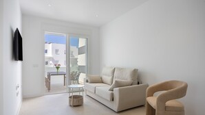 A modern living room with a sofa, a chair, a small table, and a TV mounted on the wall. - Apartment 'Los Drogos, Building A, First A' with Shared Pool, Garden and Wi-Fi (Chiclana de la Frontera)