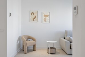 Ein schlicht eingerichteter Raum mit einer Couch, einem Sessel, einem kleinen Tisch und zwei gerahmten Kunstwerken an der Wand.