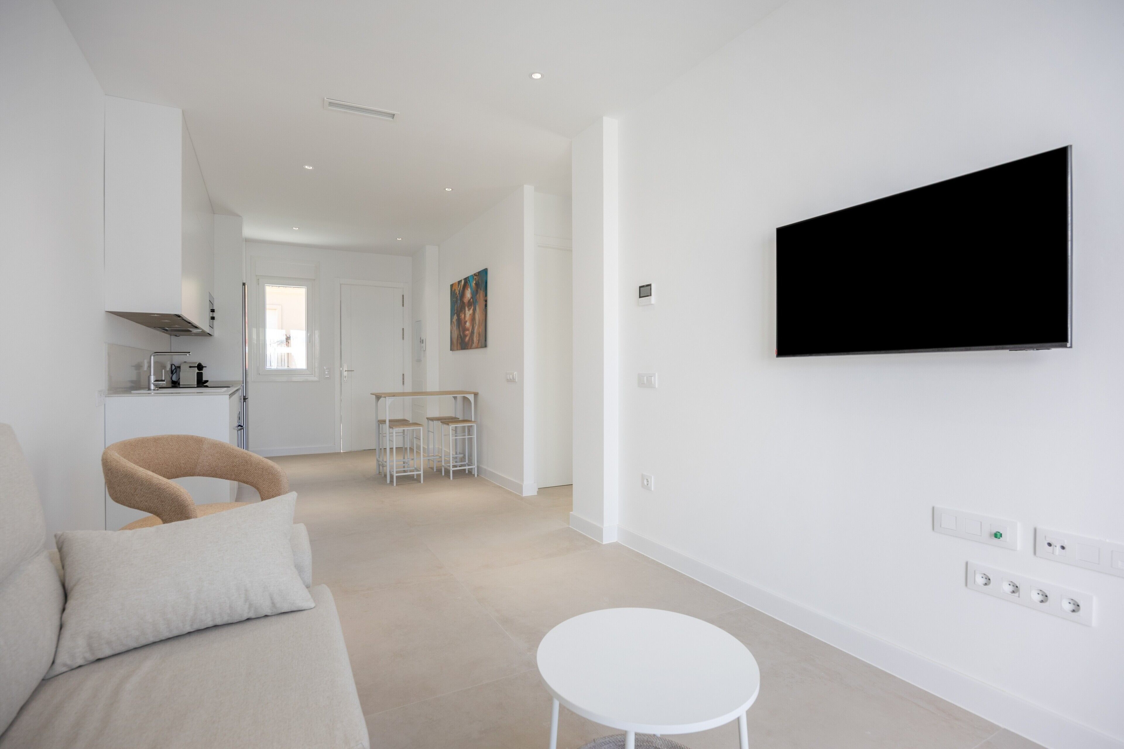 A modern living room with a sofa, a round white table, and a flat-screen TV mounted on the wall.