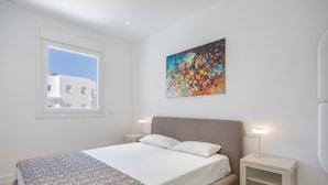 A bedroom with a bed, a window, a painting, and bedside lamps. - Apartment 'Los Drogos, Building A, First C' with Shared Pool, Garden and Wi-Fi (Chiclana de la Frontera)