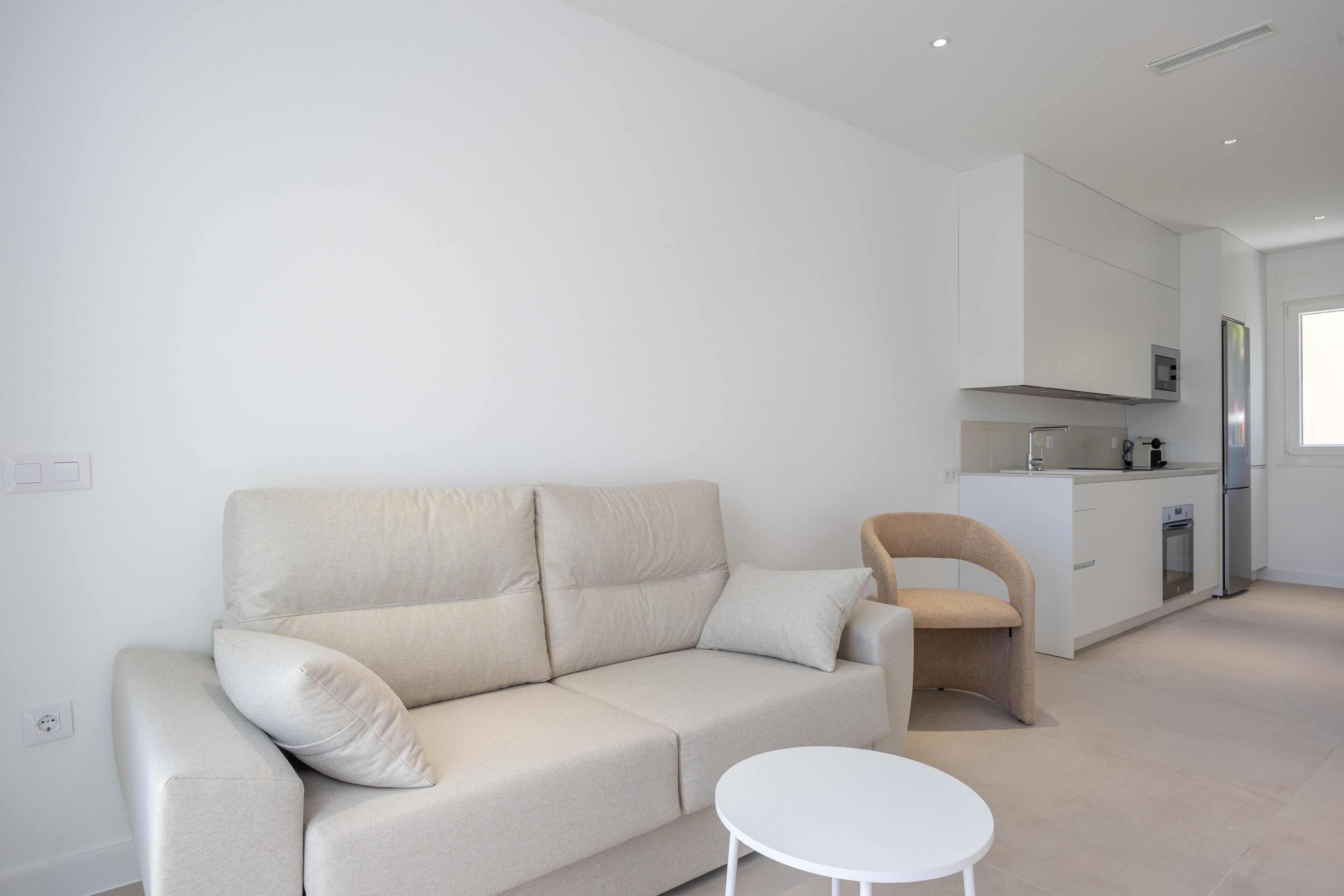 A modern living room with a sofa, a small round table, and a kitchen area in the background.