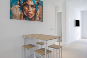 Un interior modern amb una taula de fusta i quatre tamborets, un quadre abstracte gran a la paret, i un televisor fixat a la paret.