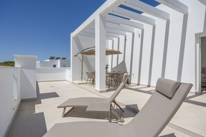 Eine Dachterrasse mit Liegestuhl, Tisch mit Stühlen und einer Pergola mit Sonnenschirmen.
