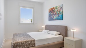 A bedroom with a bed, bedside tables, a window, and a painting on the wall. - Apartment 'Los Drogos, Building B, Penthouse B' with shared pool, garden & Wi-Fi (Chiclana de la Frontera)