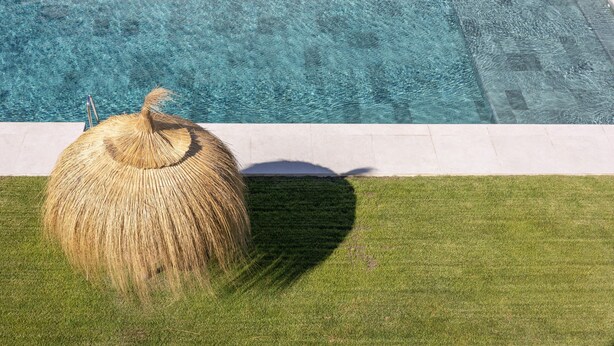 Uma piscina azul cristalina com área gramada e estrutura de palha.