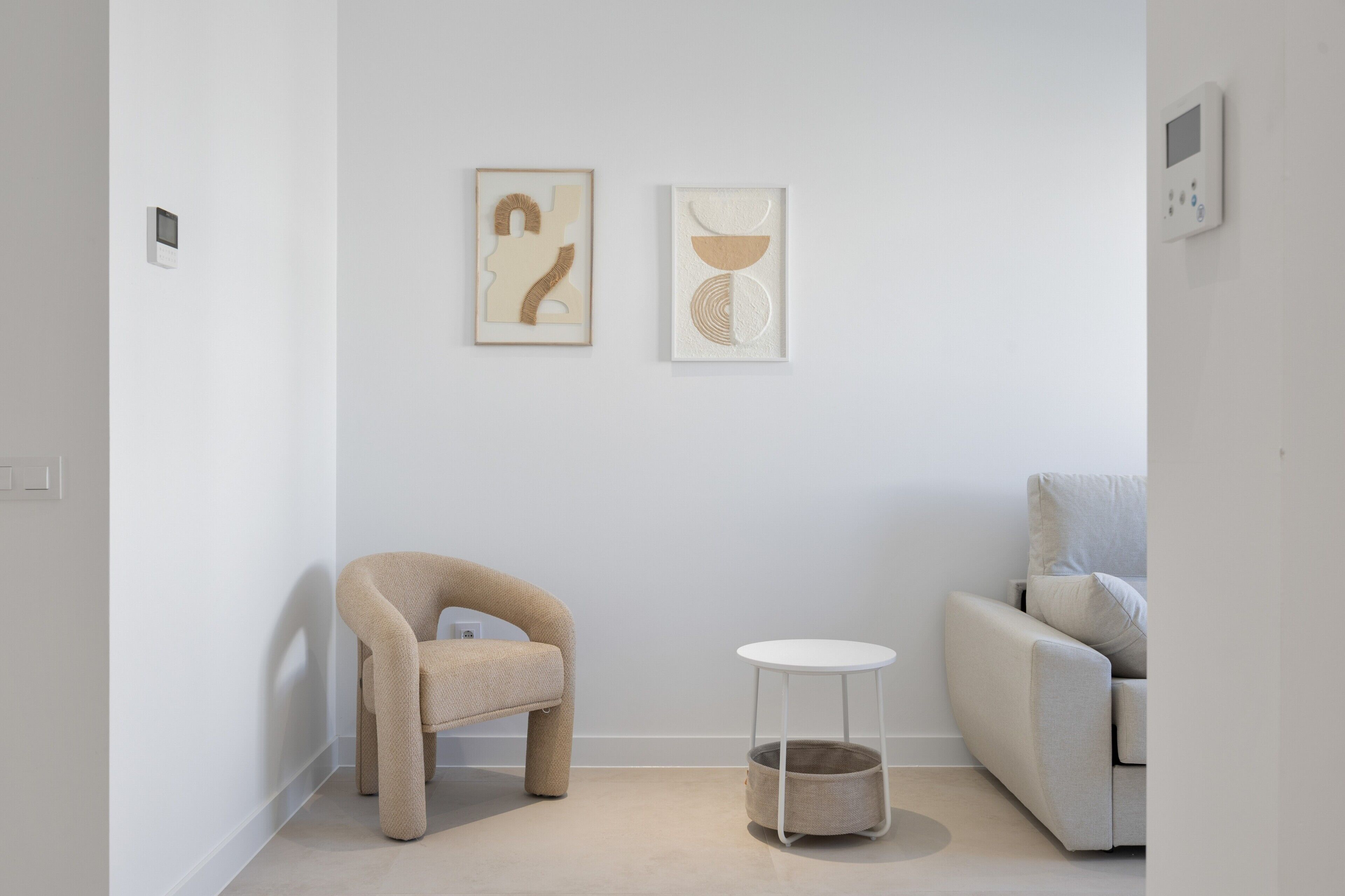 Une pièce au décor minimaliste, avec un canapé, un fauteuil, une petite table et deux œuvres d’art encadrées accrochées au mur.