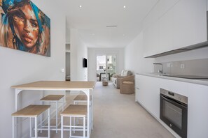 Une cuisine moderne avec des meubles blancs, un four encastré et un coin repas comprenant une table en bois et des tabourets.