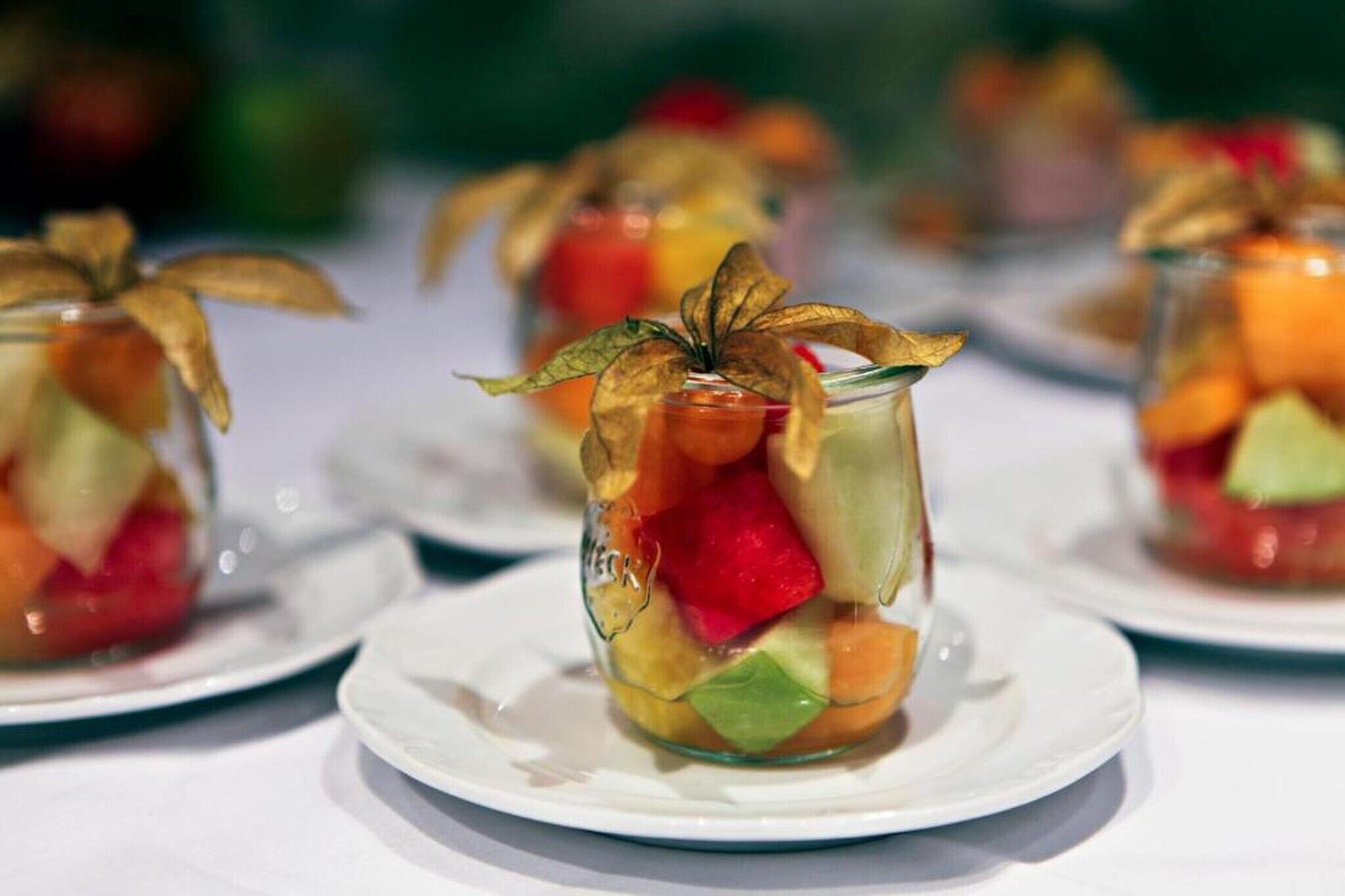 En dessert i ett glas, med frukt och ett dekorativt blad, serverad på en vit tallrik.