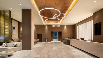 Un moderno vestíbulo de hotel con recepción, zona de estar y un diseño de techo único.