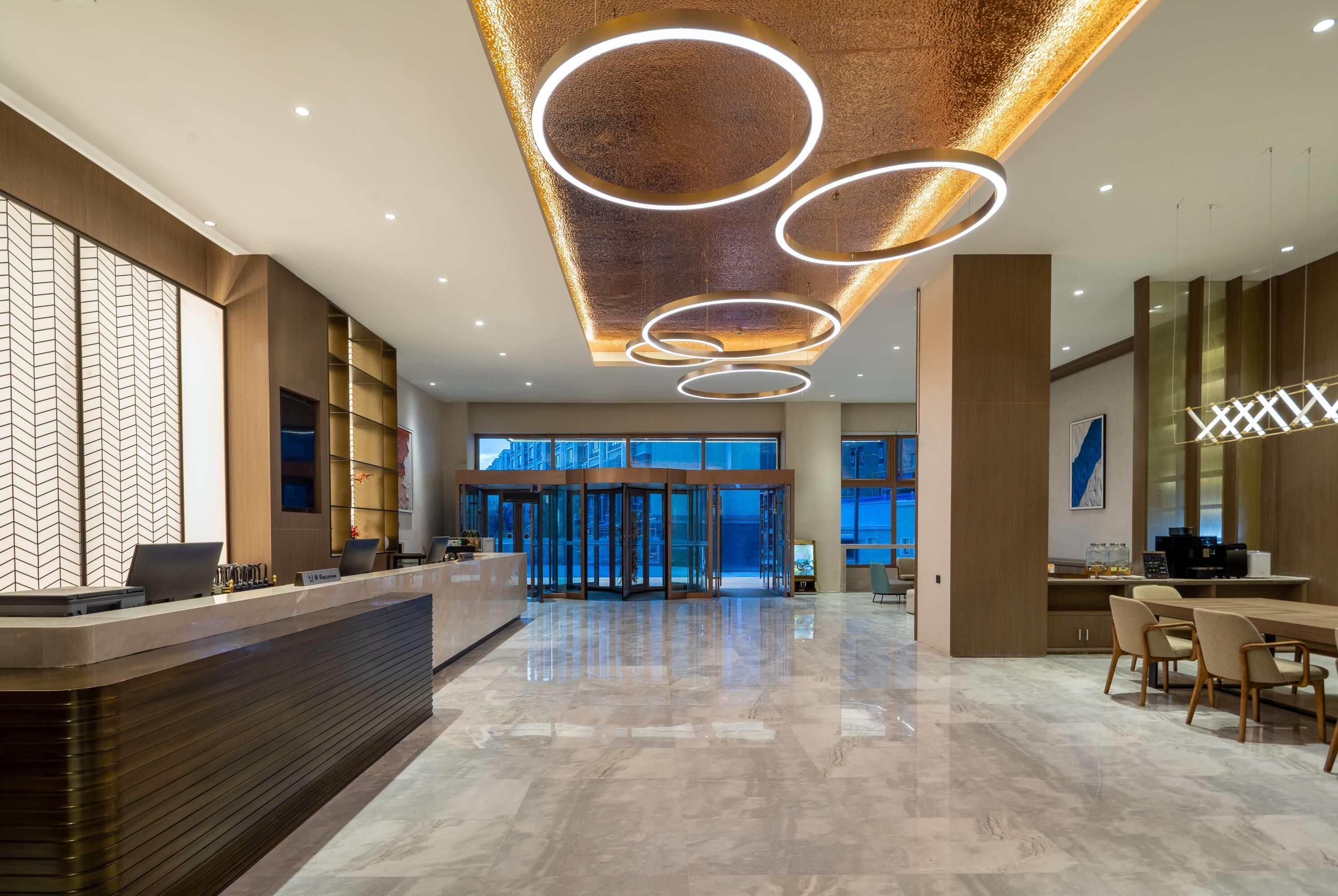A modern hotel lobby with a reception desk, a glass elevator, and a seating area.