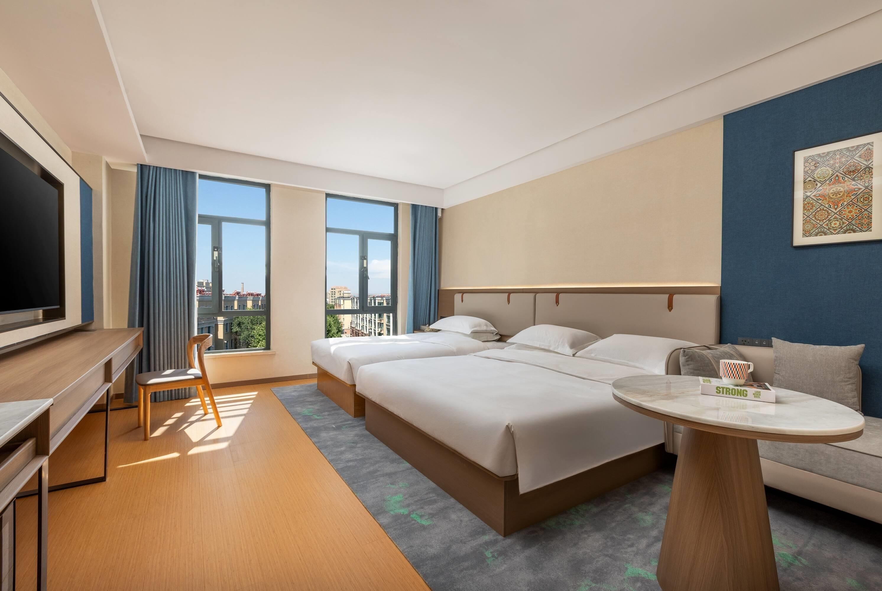 A hotel room with a bed, a TV, a desk, and a view of the city.