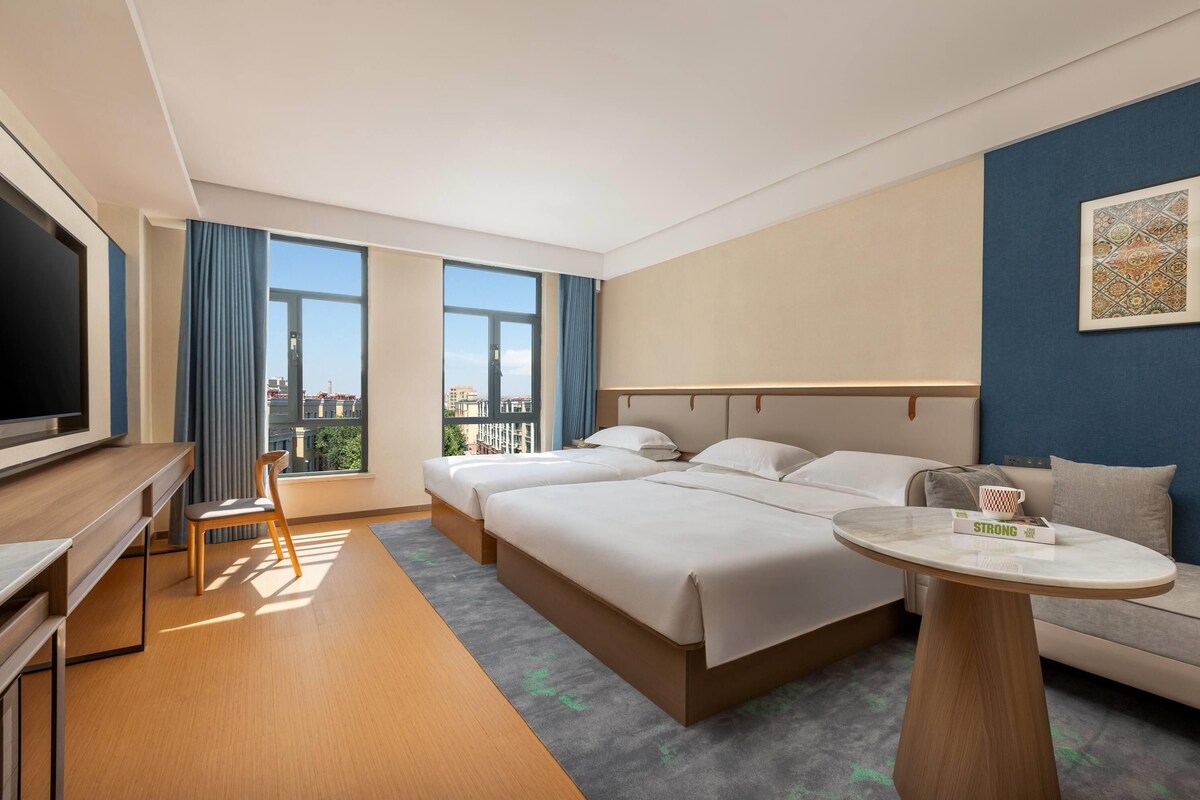 Hotellihuone, jossa on sänky, työpöytä, tuoli, televisio ja näkymä kaupunkiin.