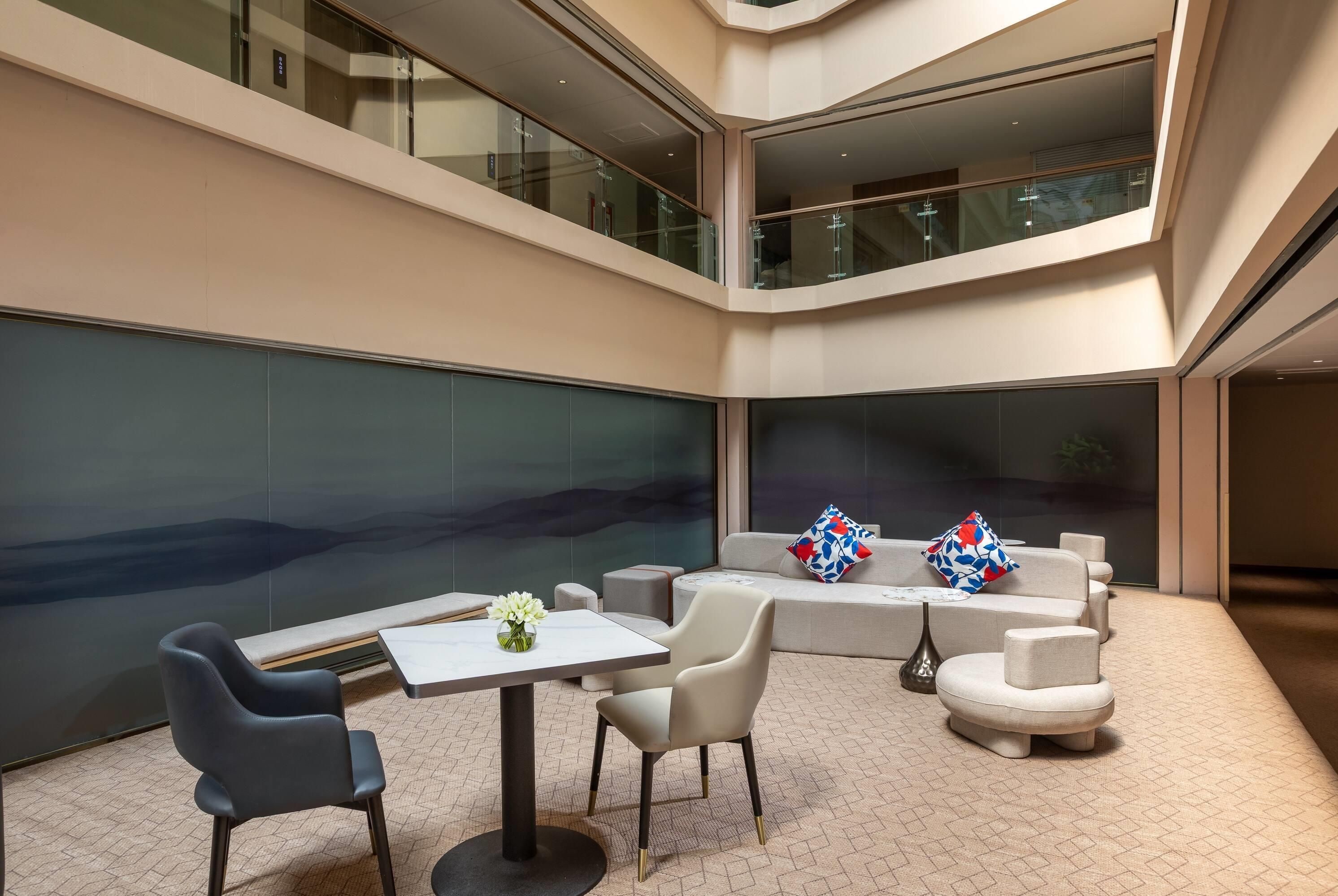 Ein großzügiges, mehrgeschossiges Atrium mit einer Sitzgruppe, bestehend aus einer Couch, Sesseln, einem kleinen Tisch und dekorativen Kissen.