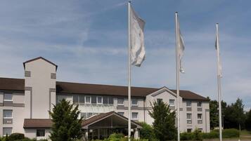 Et hotel med flere etager, en central indgang, flagstænger og en anlagt have.