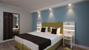 A modern hotel room with a large bed, bedside tables, a mirror, and a wardrobe.