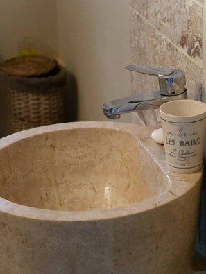 A bathroom with a marble sink, a white ceramic mug labeled 'LES BAINS,' and a metal faucet.