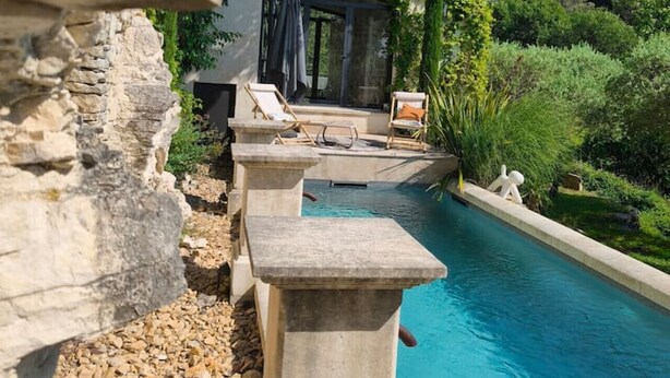 A poolside area with stone steps, lounge chairs, and a view of a house with a covered patio.