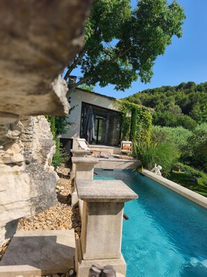 Ein Poolbereich mit Steintreppe, Liegestühlen und Blick auf ein Haus mit einer überdachten Terrasse.