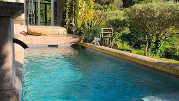 A swimming pool with a clear blue water, surrounded by greenery and a building with a glass door.