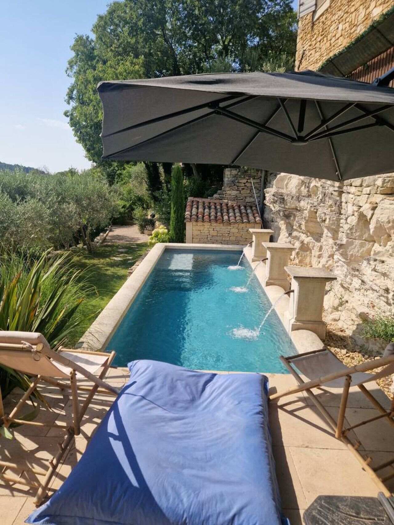 A swimming pool with a stone wall, a pergola, and lounge chairs.