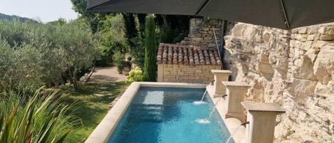 A swimming pool with a stone wall, a pergola, and lounge chairs.
