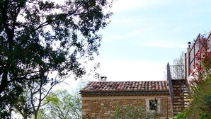 A stone house with a tiled roof, a gravel path, and surrounding vegetation.