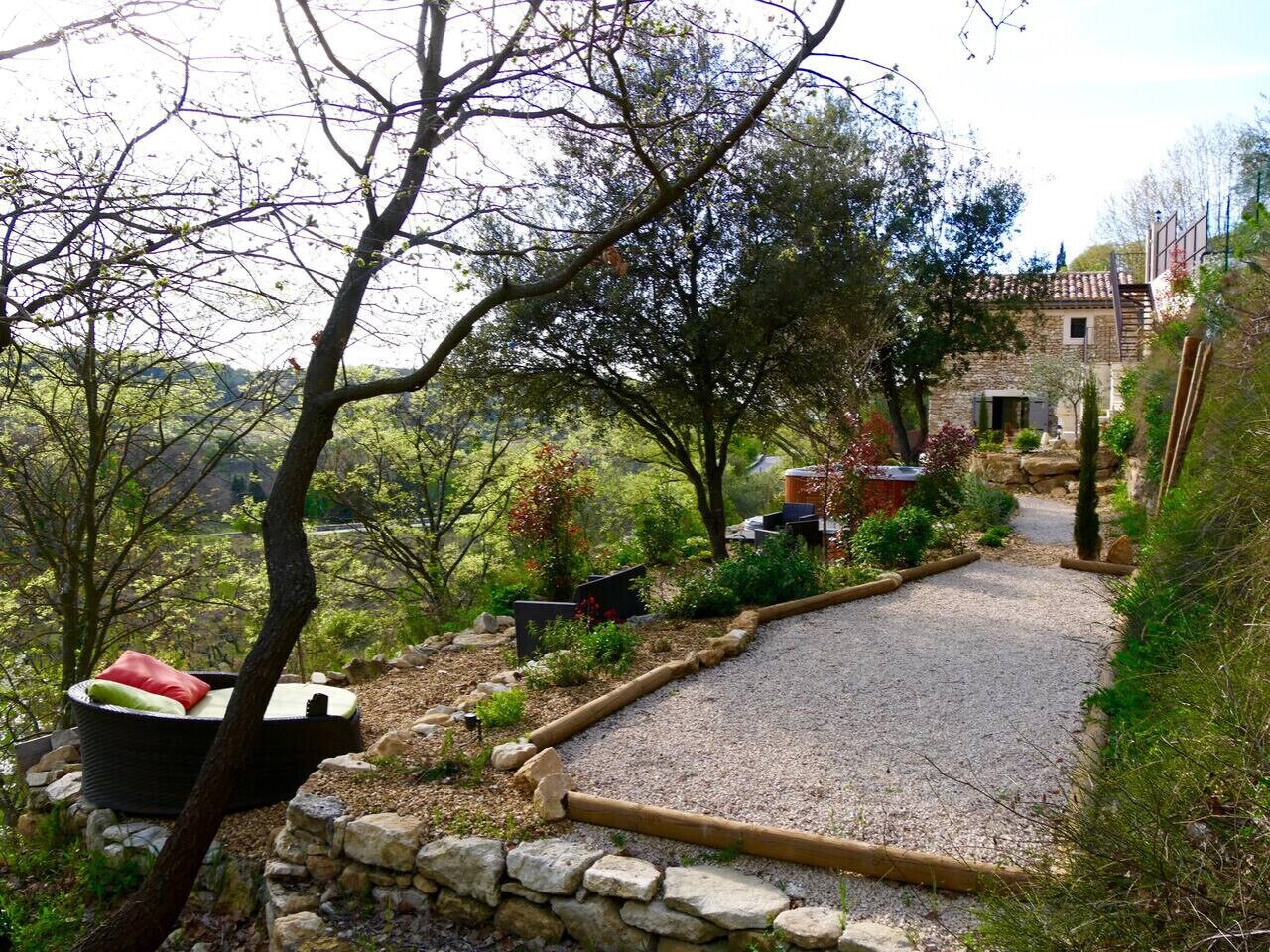 A stone pathway leading to a rustic stone building, surrounded by trees and greenery.