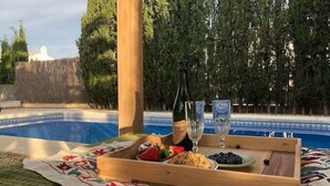 Ein Holztablett mit Speisen und Getränken am Pool, umgeben von Bäumen und einem Zaun.