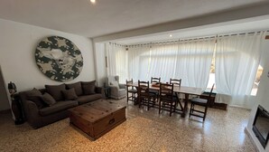 Ein Wohnzimmer mit einer Couch, einem Couchtisch, einem Esstisch, Stühlen und einem großen Wandbild.