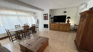 Ein Wohnzimmer mit Couchtisch aus Holz, Esstisch mit Stühlen, Fernseher und Kamin.