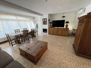 Ein Wohnzimmer mit Couchtisch aus Holz, Esstisch mit Stühlen, Fernseher und Kamin.
