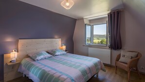 Une chambre à coucher avec un lit, des tables de chevet, une chaise, une fenêtre et une vue sur l’extérieur.