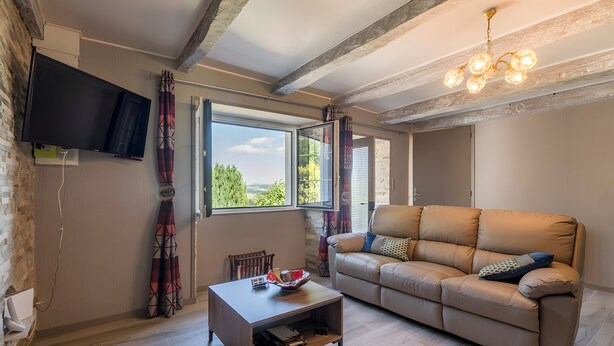Un salon comprenant un canapé, une table basse, un téléviseur fixé au mur et une fenêtre avec des rideaux.