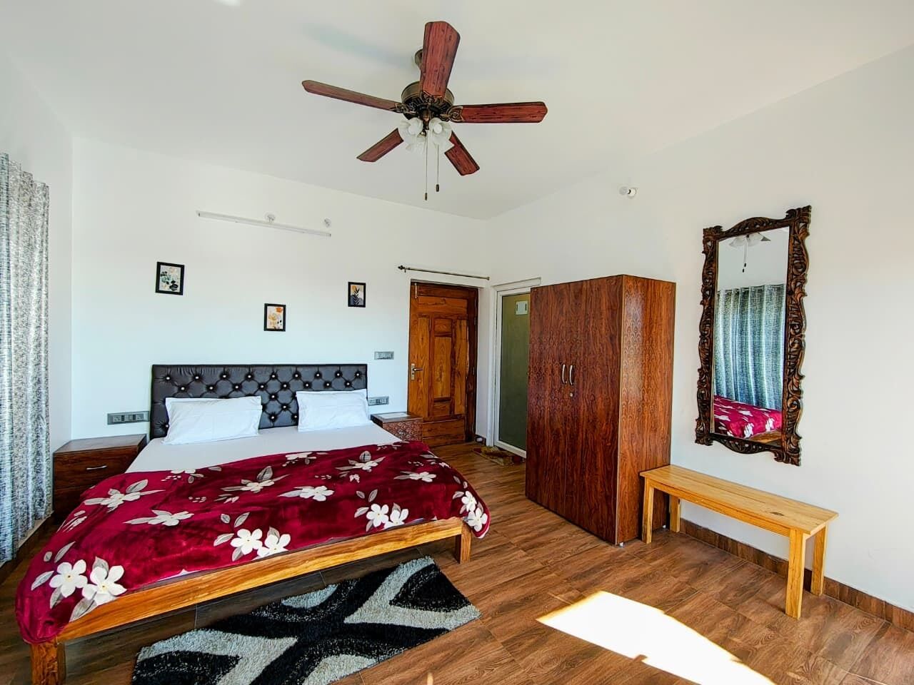Una camera da letto con un letto, un'armadiatura in legno, una panca, una ventola a soffitto e uno specchio.