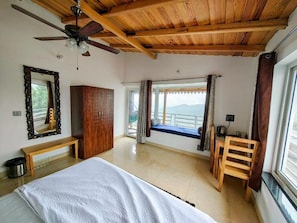 A bedroom with a bed, wooden ceiling, a bench, a wardrobe, a window with curtains, and a view of the outdoors. - Abhi's Cottage (Mukteshwar)